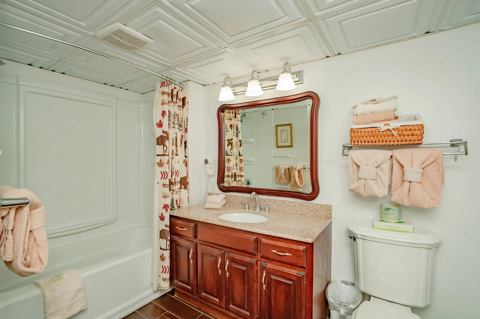 Step into a beautifully appointed bathroom with elegant wood cabinetry, a granite-topped vanity, and soft peach towels ready for your arrival. The detailed coffered ceiling adds a touch of charm to your morning routine.