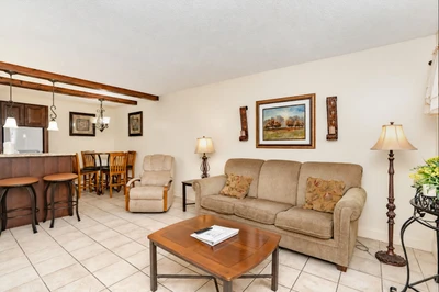 Step into your open-concept retreat where warm wood tones and comfortable furnishings create an inviting space to unwind. The living area flows seamlessly into your dining nook and kitchen, perfect for relaxing evenings at home.