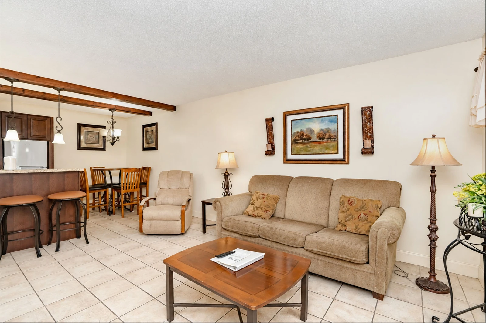Step into your open-concept retreat where warm wood tones and comfortable furnishings create an inviting space to unwind. The living area flows seamlessly into your dining nook and kitchen, perfect for relaxing evenings at home.