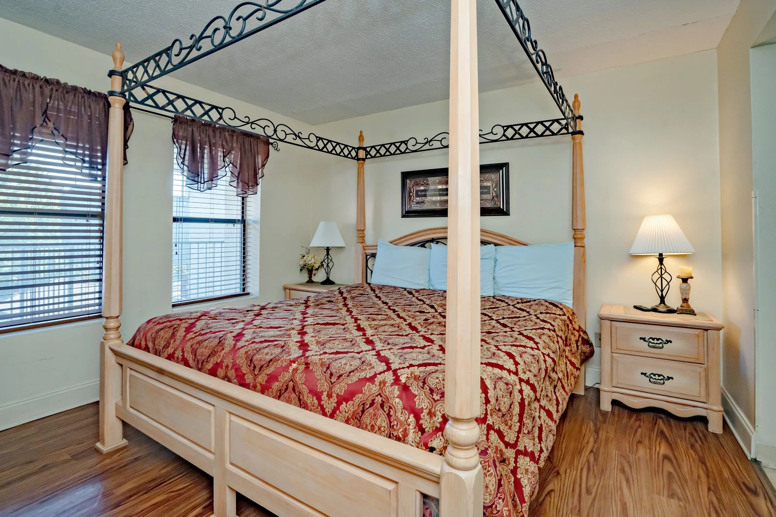 Step into your elegant bedroom featuring a romantic four-poster bed dressed in rich red and gold linens. Natural light filters through the windows while bedside lamps create a warm, inviting glow for your restful retreat.