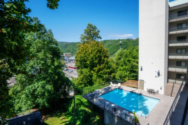A scenic aerial view of the property showcases the outdoor swimming pool surrounded by lush greenery and forested hillsides, with the town nestled in the valley below.