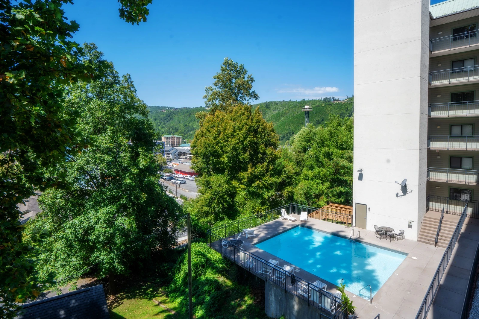 A scenic aerial view of the property showcases the outdoor swimming pool surrounded by lush greenery and forested hillsides, with the town nestled in the valley below.