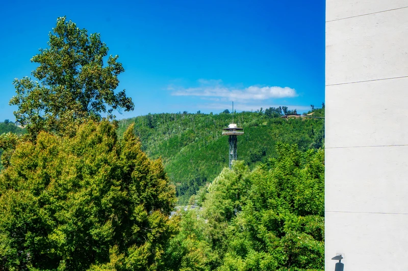 The property is situated in a naturally scenic area with lush green hillsides and a landmark observation tower visible in the surrounding landscape.