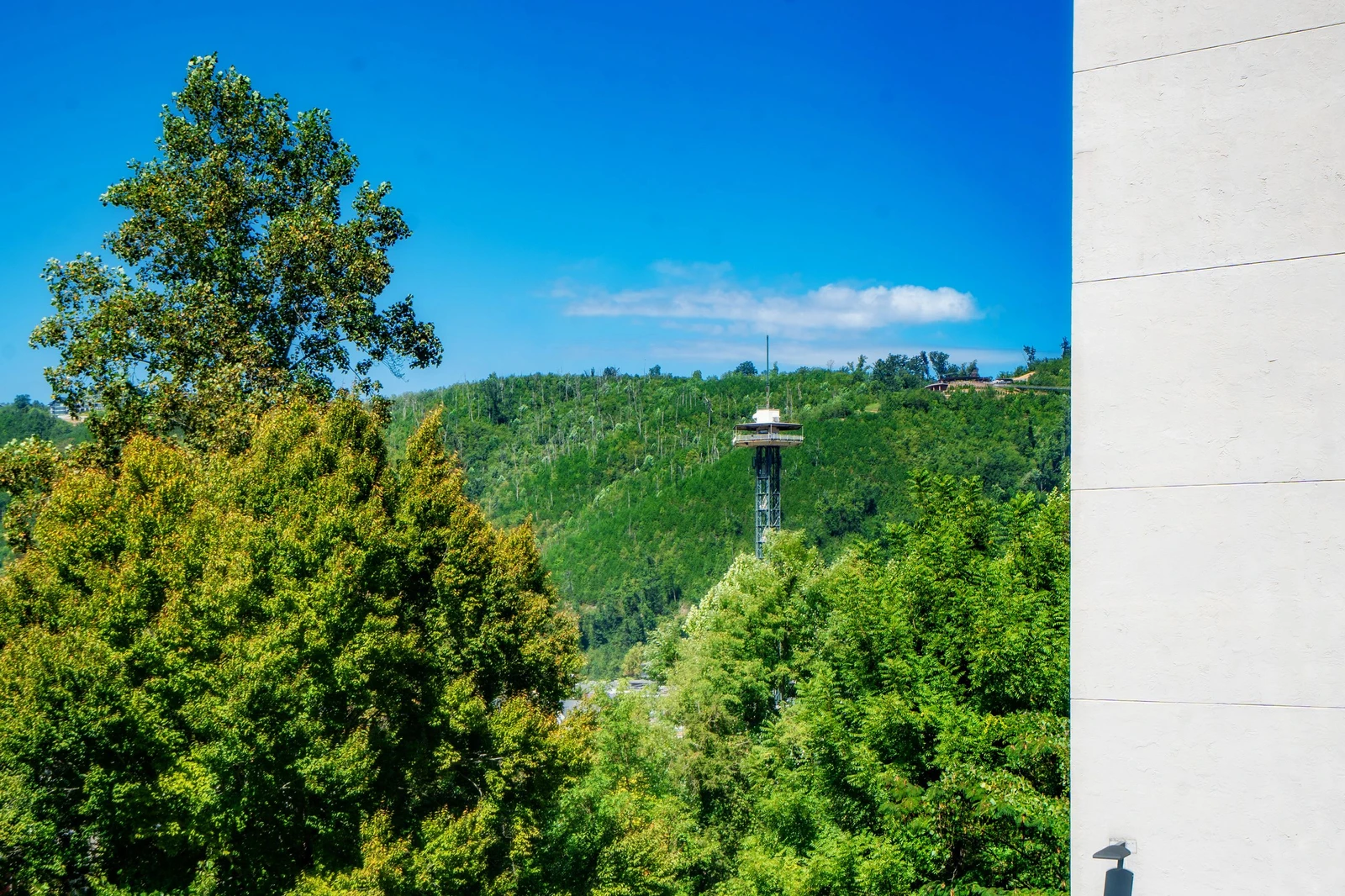 The property is situated in a naturally scenic area with lush green hillsides and a landmark observation tower visible in the surrounding landscape.