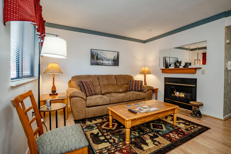 Settle into your cozy living space featuring a warm fireplace, plush sofa, and natural light streaming through the windows—your perfect retreat after a day of mountain adventures.