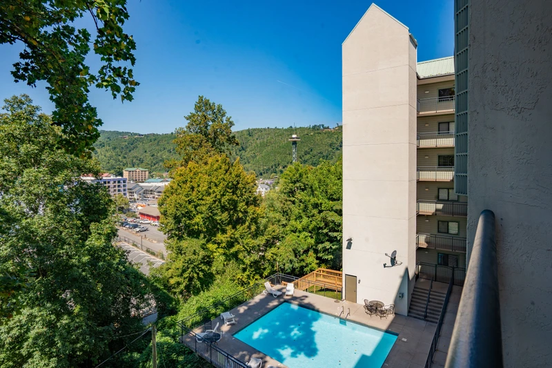 The property features a sparkling swimming pool surrounded by lounge chairs and mountain scenery, set in a wooded hillside location with convenient access to nearby town amenities.