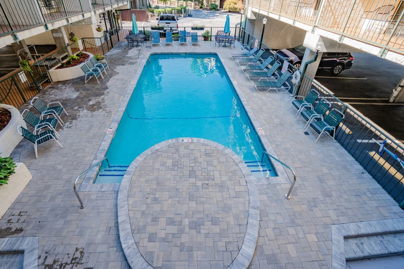 The property features a refreshing outdoor pool area with ample lounge seating, surrounded by paver decking and convenient parking nearby.