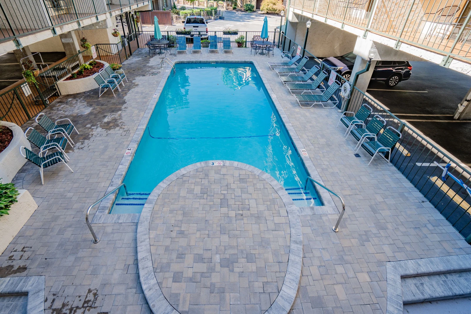 The property features a refreshing outdoor pool area with ample lounge seating, surrounded by paver decking and convenient parking nearby.