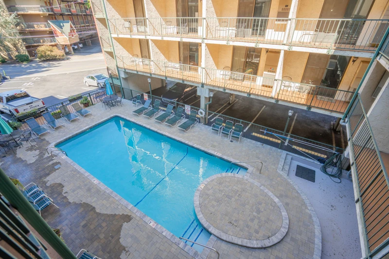 The property's courtyard pool and loungers, surrounded by guest room balconies and a nearby parking area, creating a central relaxation space for visitors.